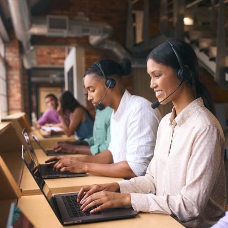Multi-Cultural Customer Support Or Telesales Team In Modern Open Plan Office Wearing Headsets